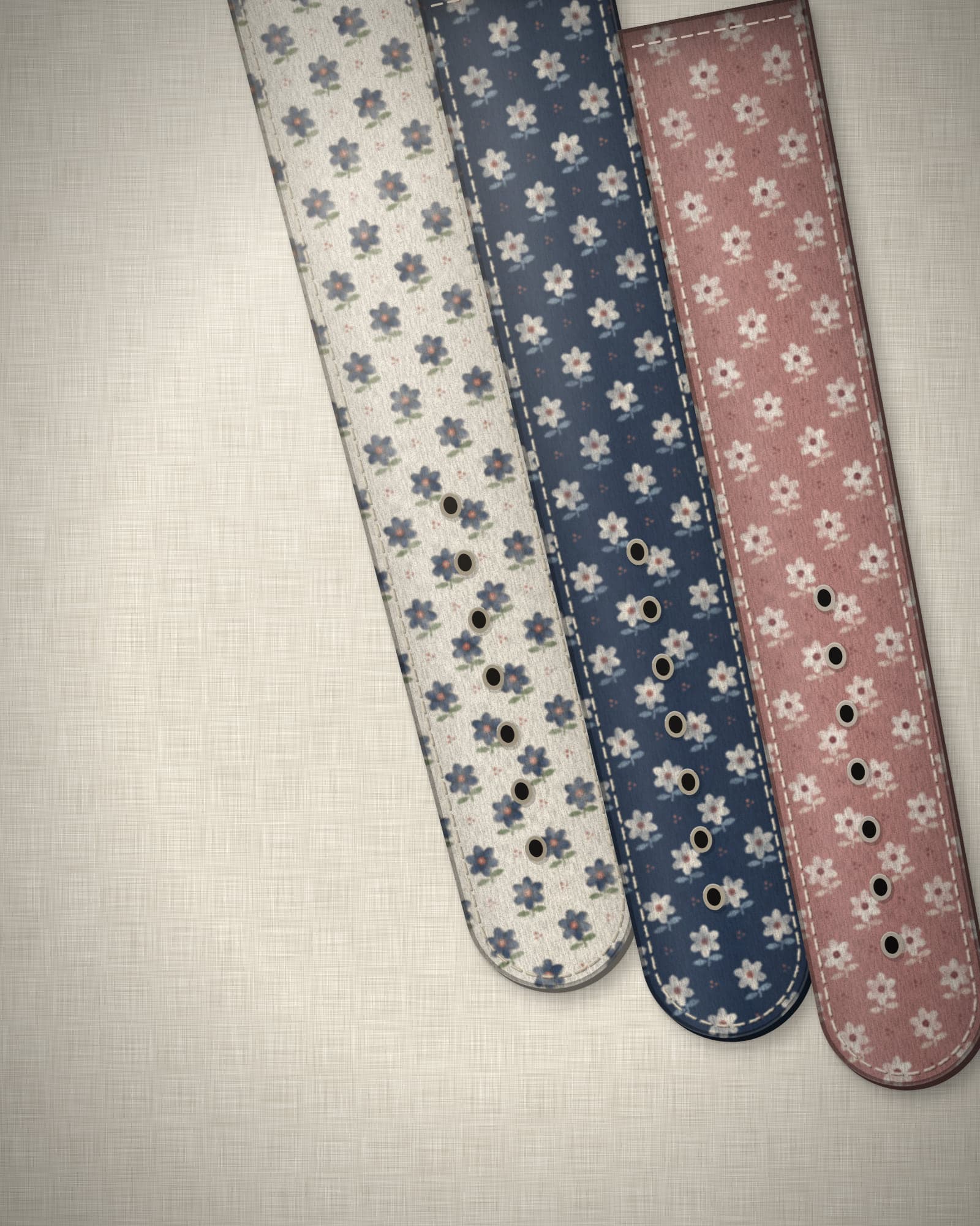 Three concept straps — ivory, indigo and rose floral prints — laid in parallel on natural linen.